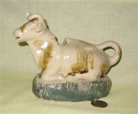 Heavy ceramic kneeling brown cow creamer on thick green base
