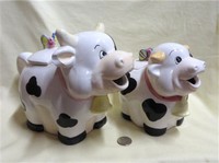 Two happy pudgy cow teapots with bugs on lids