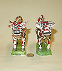 Two red and black splatter painted cow creamers on green bases, front