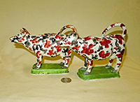 Two red and black splatter painted cow creamers on green bases, side