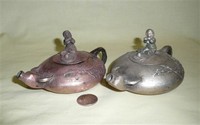Two Chinese flatish metal water buffalo teapots with boys playing flutes on top