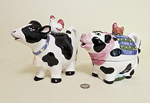 Two black and white cow teapots with birds on lids